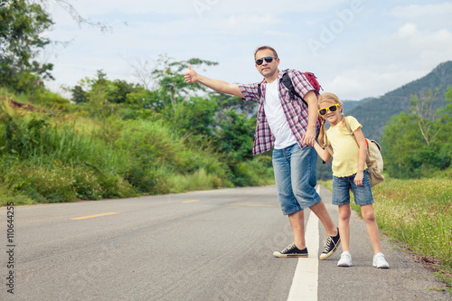 Father and daughter walking on the road at the day time.