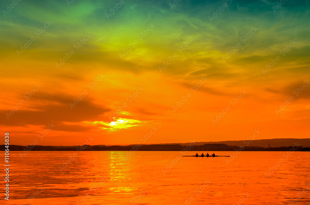 Rowers in a rowing boat silhouette on sunset background in lake