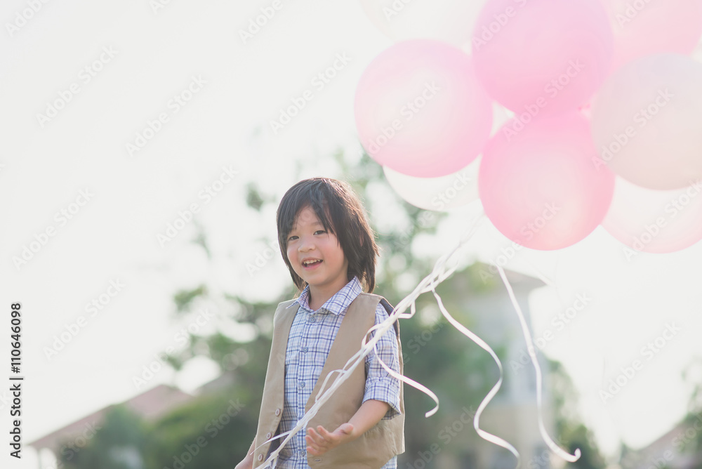 Cute Asian child with many balloons playing in the park under su