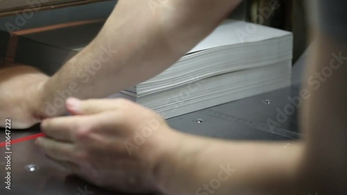 Modern paper guillotine cutter works in a printing company. By machinery warning sign pasted on safety.