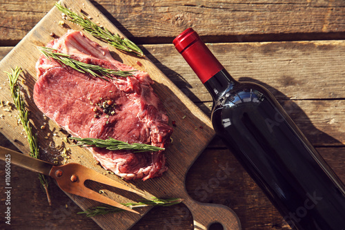 Cuadro en lienzo Raw pork steak with bottle of red wine, meat fork and rosemary on wooden backgro