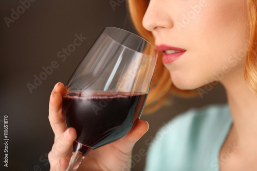 Young woman with glass of red wine on light blurred background