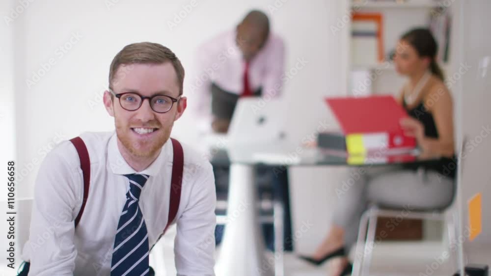 Portrait smiling businessman in office with colleagues working in background Portrait smiling businessman in office with colleagues working in background