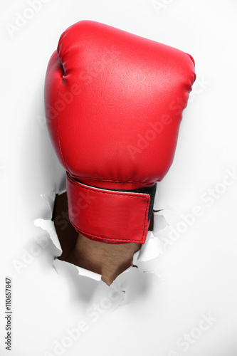 Male hand in boxing glove through white paper, isolated on white