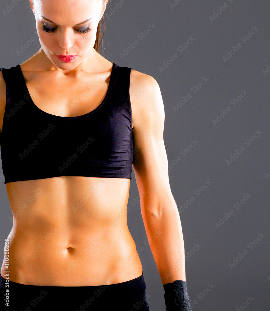 Muscular young woman standing on gray background Muscular young woman standing on gray background