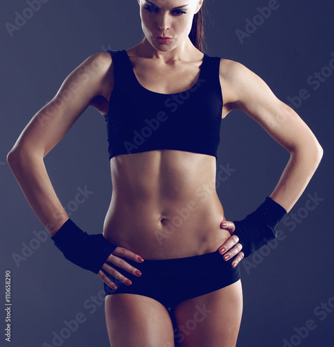 Muscular young woman standing on gray background