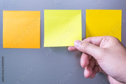 Close-up Of Person's Hand Holding Blank Yellow Note Sticked On Fridge Door
