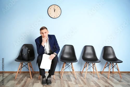 Young man in suit sitting on chair and waiting for job interview