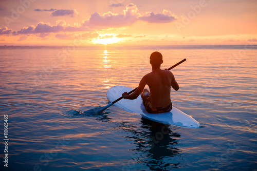 Silhouette of man paddleboarding at sunset photo