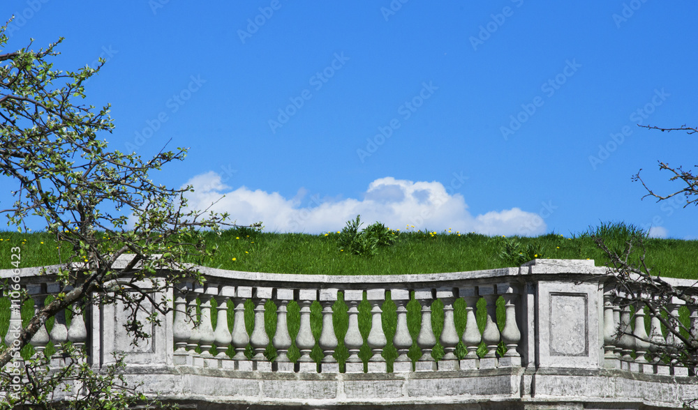 Balustrade on the background of green grass lawn and blue sky with clouds