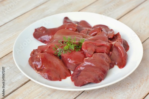 Raw liver on the white plate on the wooden background