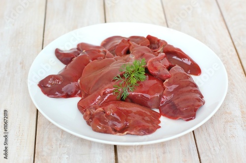 Raw liver on the white plate on the wooden background