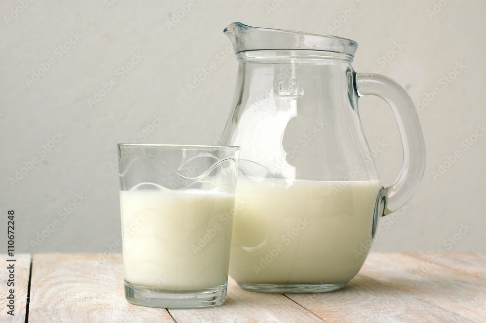 White milk in the glass with the jug on the wooden background White milk in the glass with the jug on the wooden background