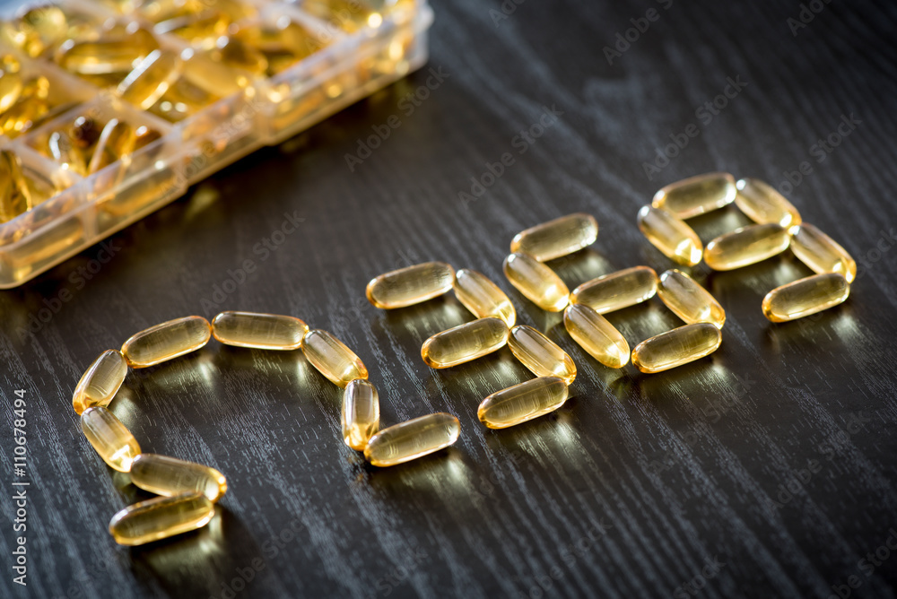 Omega 3-6-9 fish oil yellow softgels drawing omega 3-6-9 letters on wooden black table. Daily pill box. Omega 3-6-9 fish oil yellow softgels drawing omega 3-6-9 letters on wooden black table. Daily pill box.