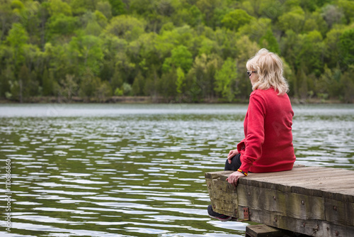 Woman sitting on a dock overlooking a lake on a spring day © frank1crayon