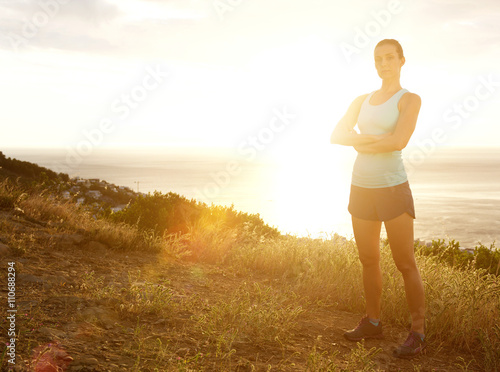 Serious sport woman with arms crossed standing in sunset