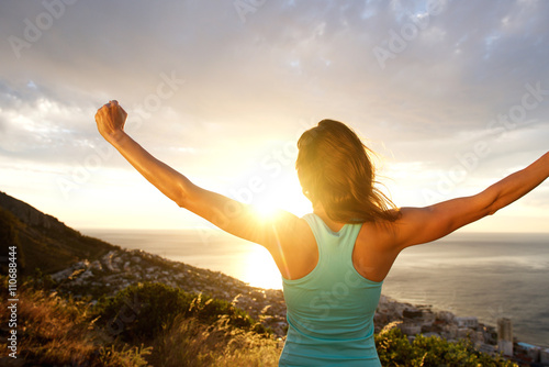 Woman from behind stretching out arms by sunrise