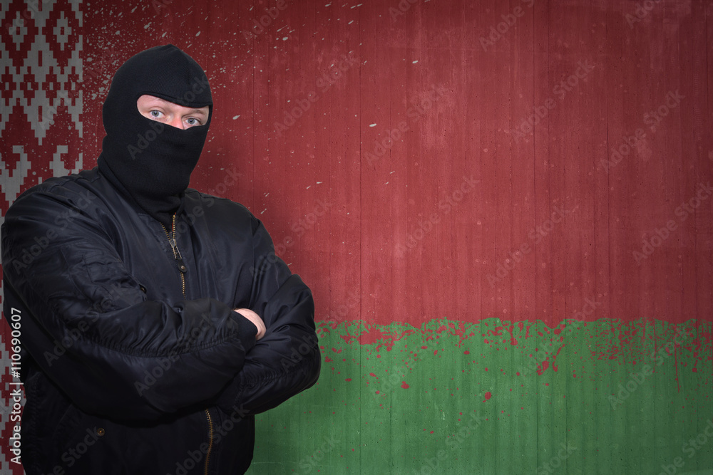dangerous man in a mask standing near a wall with painted national flag of belarus