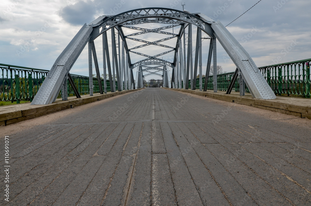 Fototapeta premium centennial metal bridge with wooden surface over Dzisna river Dzisna, Belarus