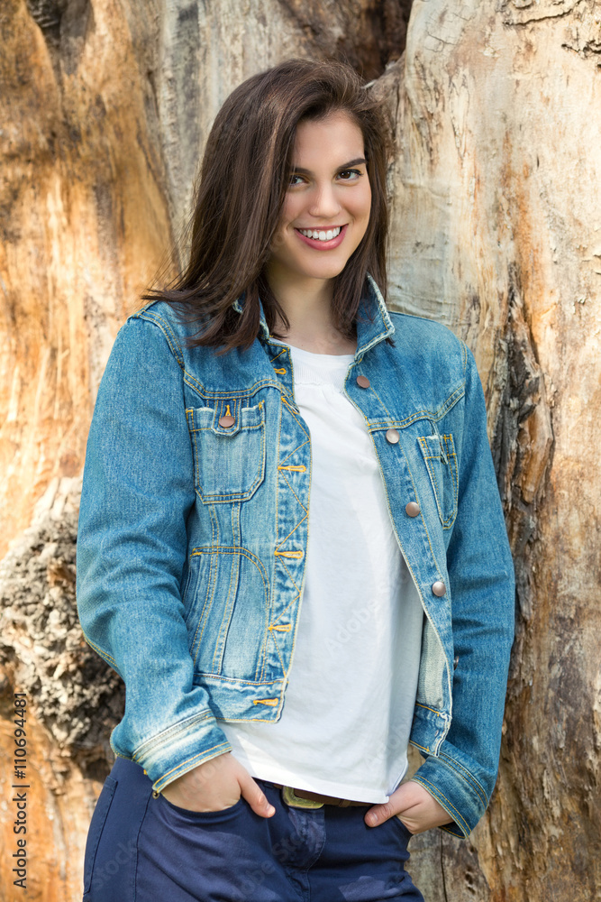 Portrait of a beautiful young woman looking at camera while leaning on a tree in a park on a nice and sunny spring day