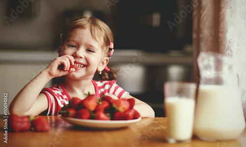Bilde på lerret happy child girl eats strawberries in summer home kitchen