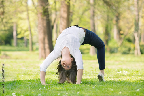 Happy young woman is doing Yoga Bridge pose in a park on a nice sunny spring day.