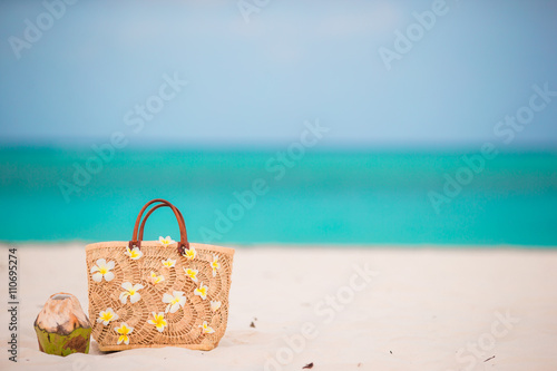 Closeup beautiful bag with frangipani flowers and coconut on white beach