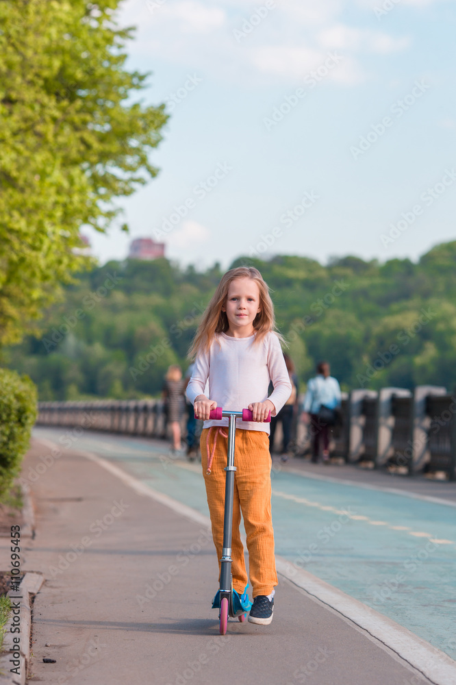 Adorable little girl riding her scooter in a summer park