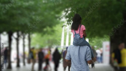 African American father and daughter walking away from camera in urban park