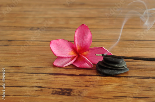 A pink frangipani flower displayed with a stack of pebbles and burning incense sticks