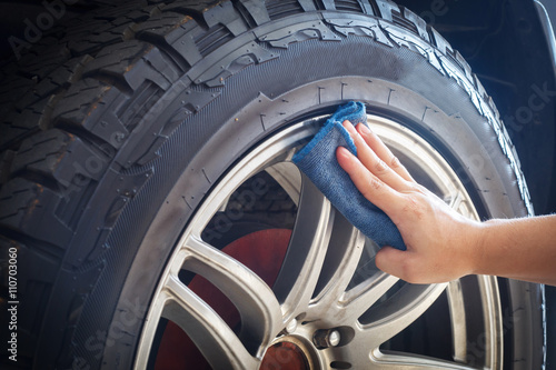Man's hand holding a blue fabric cleaning car tires and wheels