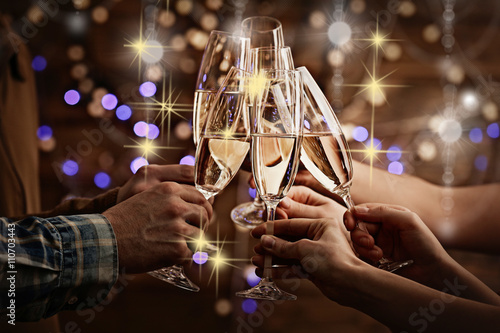 Clinking glasses of champagne in hands on bright lights background with snow effect