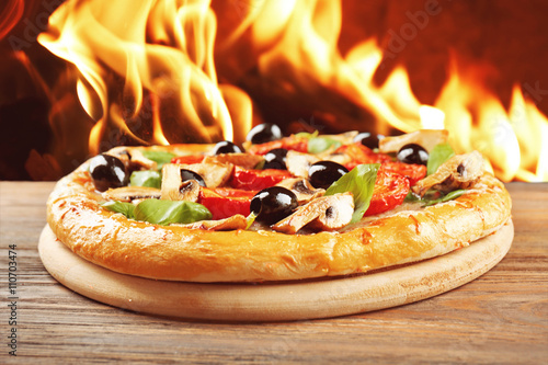 фотографія Delicious tasty pizza with ingredients on wooden table against fire flame backgr