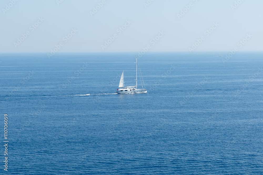 White sailboat on the blue Mediterranean Sea on the French Riviera coastline.