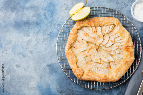Apple galette, pie, tart with cinnamon on cooling rack on a blue stone background Top view