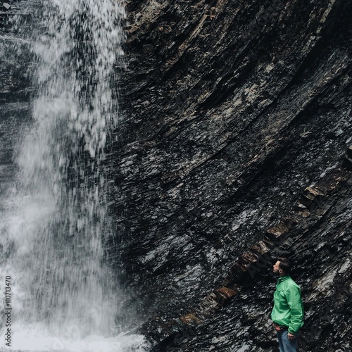 lonely man standing near waterfall in mountains