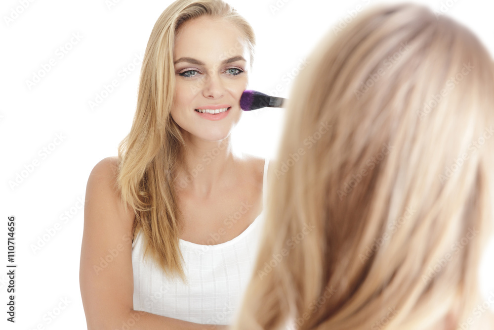 beautiful blonde woman looking into a mirror while applying blus beautiful blonde woman looking into a mirror while applying blus