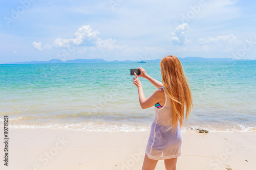 Happy attractive blonde in bikini taking a self picture on a beautiful sunny beach 