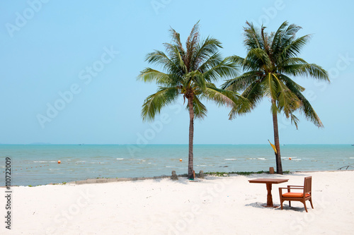 chair and table set on the white clean sand beach with coconut trees and beautiful sea.