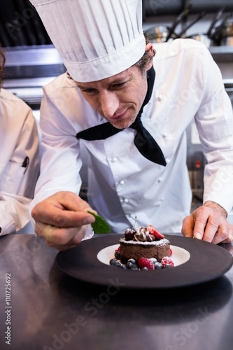 Male chef garnishing a dessert with a mint leaf on counter