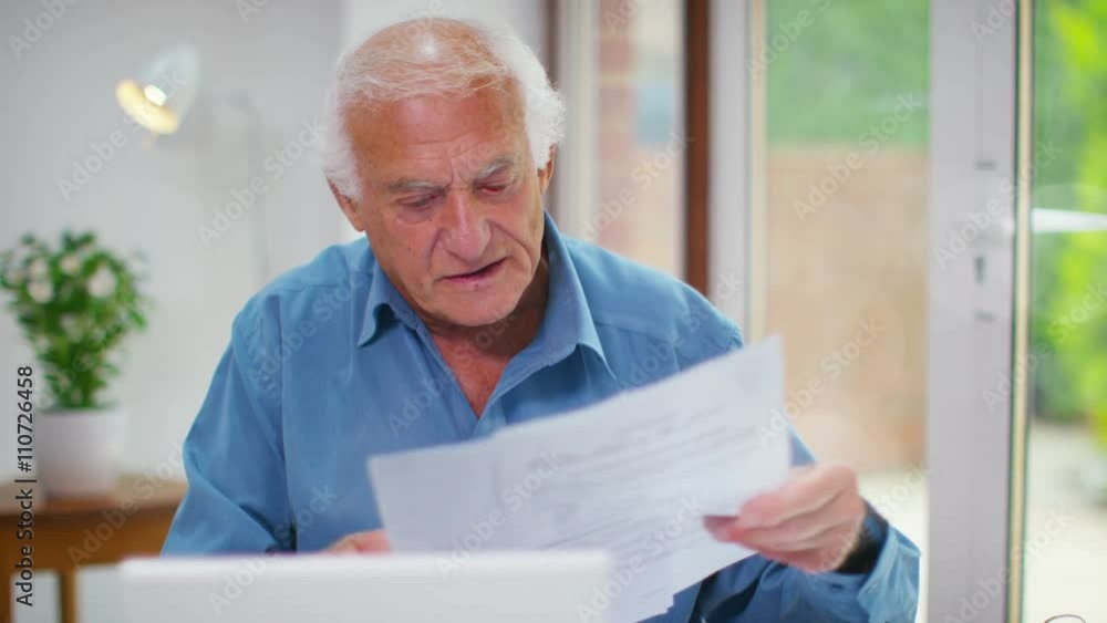 Happy senior man working on a laptop computer & looking at paperwork Happy senior man working on a laptop computer & looking at paperwork