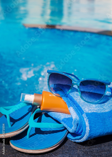 Blue slippers, sunsscreen cream and sun glasses near swimming pool - holiday concept