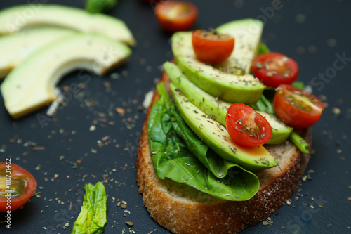 Close up of toast with spinach leaves, avocado and tomatoes.