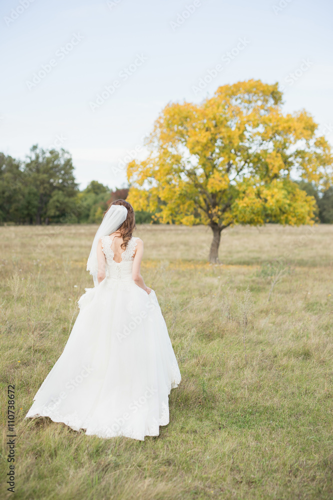 Long-haired bride in white dress walking in meadow