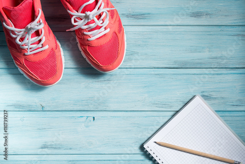 Fitness concept, pink sneakers and notebook with pencil on wooden background, top view