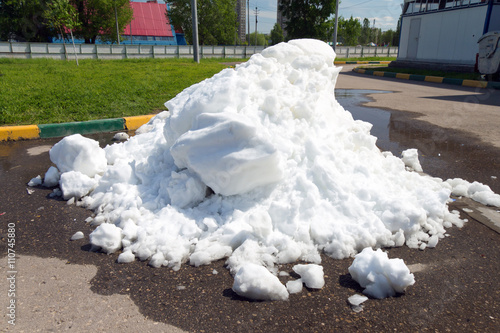 A large pile of dirty snow lying in the puddle on the asphalt ro