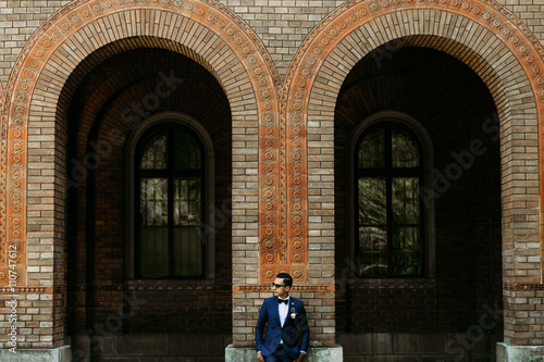Groom in the sunglasses stands next to the arch © IVASHstudio