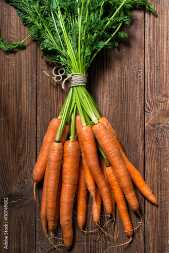 Bunch of fresh carrots with green leaves on wooden table, top view