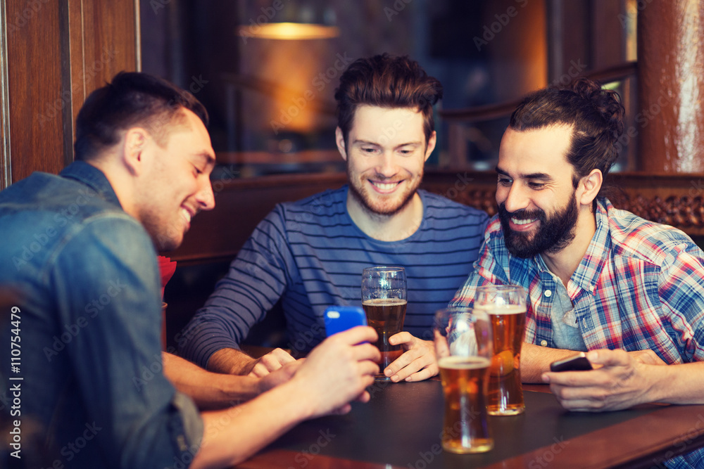 male friends with smartphones drinking beer at bar