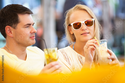 Young couple relaxing with refreshing drinks in long glasses on summer vacation with focus to an attractive woman wearing sunglasses